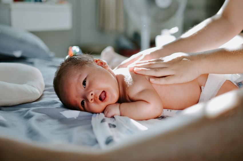 baby laying on bed while woman massaging his back