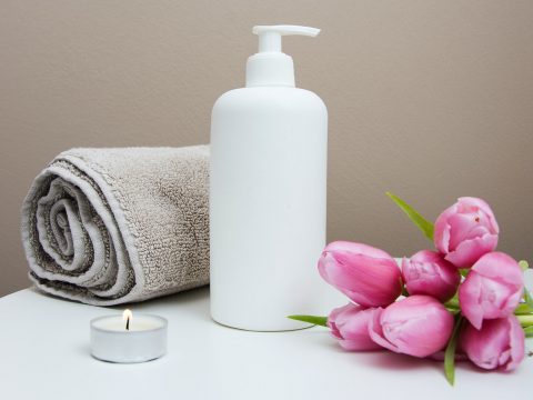 white plastic pump bottle beside pink tulips and gray towel